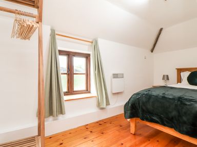 A bedroom with a bed a wooden clothing rack and a window with curtains at Keepers Cottage in Liskeard
