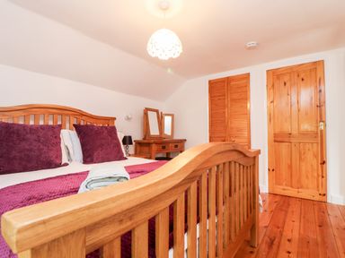 A bedroom with a wooden bed with purple pillows and blanket a wooden dressing table a wooden door and wooden closet doors at Keepers Cottage in Liskeard