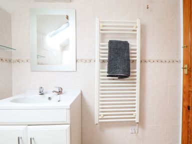 A bathroom with a sink cabinet mirror towel radiator with a gray towel and a wooden door at Keepers Cottage in Liskeard