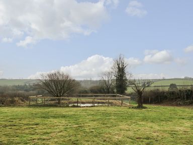 A grassy field with a fenced area containing a tree and a small pond at Keepers Cottage in Liskeard