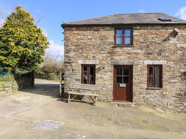 A stone cottage with wooden door and windows and a bench outside at Keepers Cottage in Liskeard