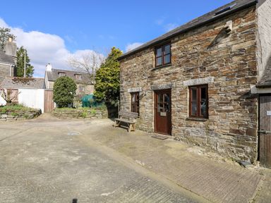 Exterior of a stone house with wooden door and windows a bench outside and other houses in the background at Keepers Cottage in Liskeard