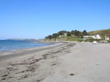 A sandy beach with seaweed near the shore with hills and houses in the background at Keepers Cottage in Liskeard