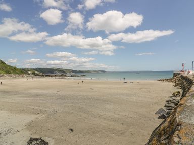 A sandy beach with people near the water and a rocky shoreline at Keepers Cottage in Liskeard