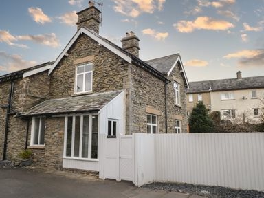 A stone house with white framed windows and a white fence at Raybarrow in Windermere