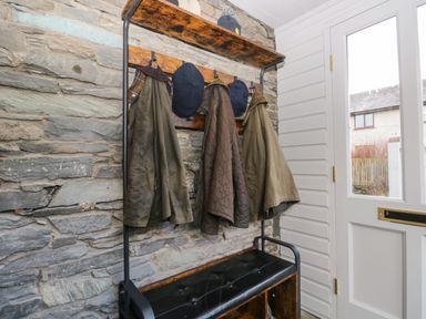 A hallway with coats and hats hanging on hooks and a bench below near a door at Raybarrow in Windermere