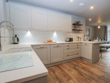 A kitchen with white cabinets wooden floor and countertop with bread kettle and toaster at Raybarrow in Windermere
