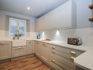 A kitchen with white cabinets wooden floor a toaster a kettle and a loaf of bread on the counter at Raybarrow in Windermere