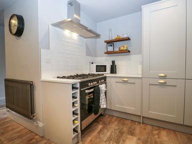 A kitchen corner with a stove oven, microwave, wine rack, floating shelves, cabinets, and a wall clock at Raybarrow in Windermere