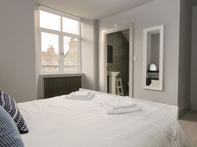 A bedroom with a bed towels on the bed a window radiator a doorway to a bathroom and a wall mirror at Raybarrow in Windermere
