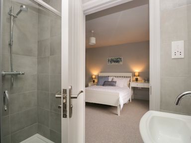 A bathroom with a shower and sink looking into a bedroom with a bed and bedside tables with lamps at Raybarrow in Windermere