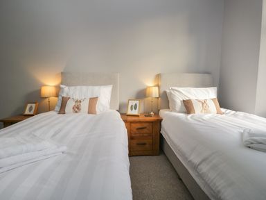 A bedroom with two single beds a wooden bedside table with lamps and framed pictures at Raybarrow in Windermere