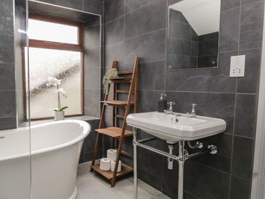 A bathroom with a white bathtub wooden shelves under a window and a white sink with a mirror at Raybarrow in Windermere