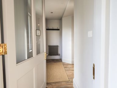A hallway with a partially open door a wall radiator a coat rack and a floor mat at Raybarrow in Windermere