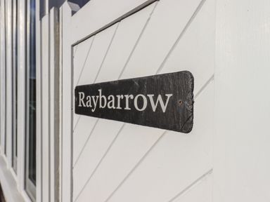 A black sign with white text reading Raybarrow on a white wooden surface at Raybarrow in Windermere