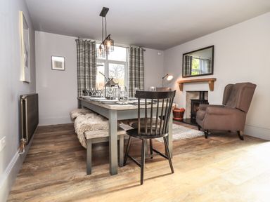A dining room with a wooden table chairs bench and fireplace at Raybarrow in Windermere