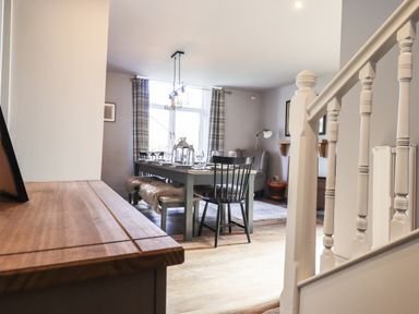 A dining area with a table set with glasses chairs and bench seats near a window with plaid curtains at Raybarrow in Windermere