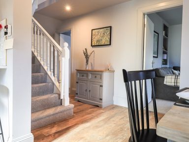 A hallway with stairs carpeted and a sideboard with a vase and painting at Raybarrow in Windermere