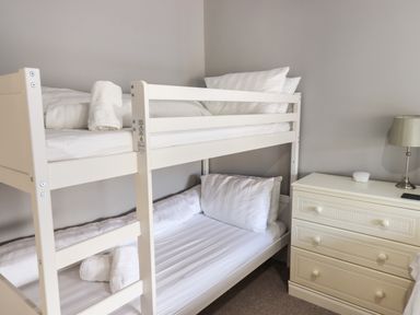 A bedroom with white bunk beds pillows and towels next to a cream chest of drawers with a table lamp at Raybarrow in Windermere