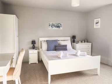 A bedroom with a white bed and white furniture including a desk chair wardrobe and chest of drawers at Raybarrow in Windermere