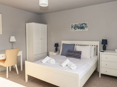 A bedroom with a white bed and blue and white pillows a white wardrobe a desk with a chair and lamps at Raybarrow in Windermere