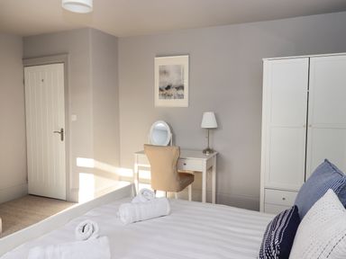 A bedroom with a bed with pillows and rolled towels a desk with a mirror and lamp a chair a white wardrobe and a door at Raybarrow in Windermere
