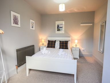 A bedroom with a white bed frame two bedside tables with lamps and wall art at Raybarrow in Windermere