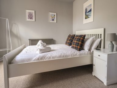 A bedroom with a white bed frame two plaid pillows folded towels on the bed a white nightstand with a lamp and three framed pictures on the wall at Raybarrow in Windermere