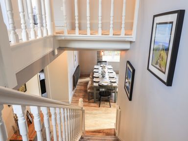 A stairway leading down to a dining area with a set table and framed pictures on the walls at Raybarrow in Windermere
