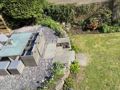An outdoor patio with a glass table and wicker chairs next to stone steps leading to a lawn at Raybarrow in Windermere