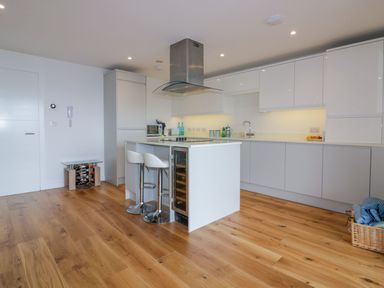 A modern kitchen with white cabinets a kitchen island with two stools and wood flooring at Onshore in Newquay