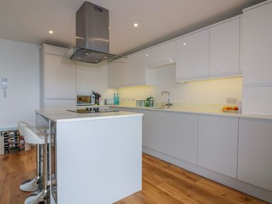 A modern kitchen with white cabinets a kitchen island with stools and wooden flooring at Onshore in Newquay