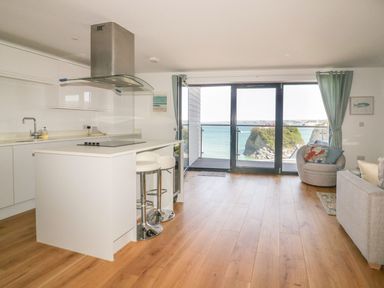 A kitchen and living area with breakfast bar stools and a balcony overlooking the sea at Onshore in Newquay