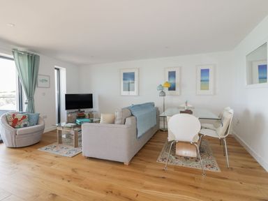 A living room with a sofa chair and tv next to a dining table and chairs at Onshore in Newquay