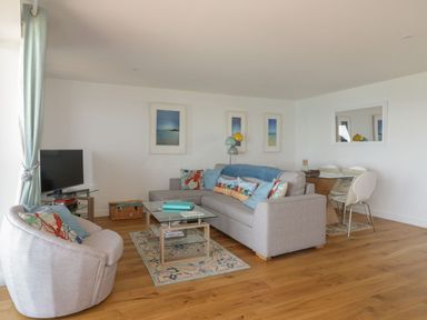A living room with a grey sofa and armchair a glass coffee table and a dining table with chairs at Onshore in Newquay