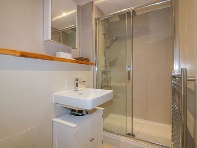 A bathroom with a white sink cabinet a glass shower enclosure and a wall-mounted mirror at Onshore in Newquay