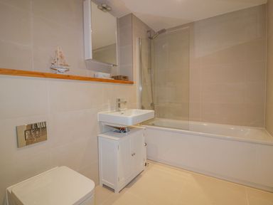A bathroom with a toilet sink cabinet bathtub and a glass shower screen at Onshore in Newquay