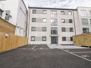 A parking area with numbered spaces in front of a modern four-story apartment building at Onshore in Newquay