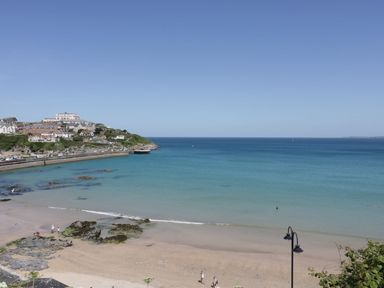 A beach with clear water and people walking near the shore with houses on a hillside at Onshore in Newquay