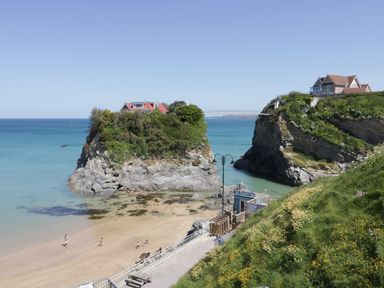 A beach with people near rock formations and houses connected by a bridge at Onshore in Newquay