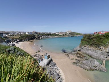 A sandy beach with people near water and rocky cliffs with houses on the hills at Onshore in Newquay
