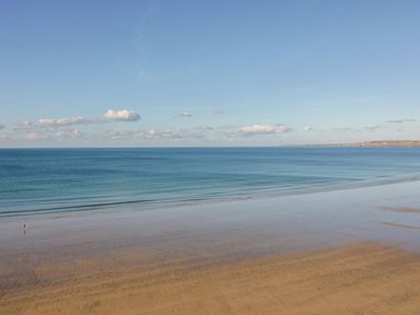 A beach with shallow water and a person walking near the shore under a blue sky at Onshore in Newquay