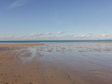 A sandy beach with shallow water and footprints under a blue sky at Onshore in Newquay