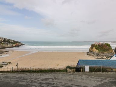 A sandy beach with people near the water and buildings on rocky hills at Onshore in Newquay
