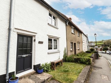 A row of cottages along a street with a small garden and bench outside Lavender Cottage in South Zeal