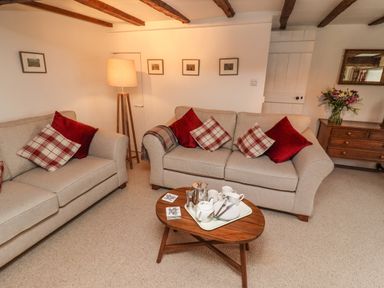 A living room with beige sofas and red and plaid cushions a wooden coffee table with tea set a floor lamp and a wooden chest with flowers at Lavender Cottage in South Zeal