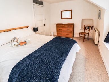 A bedroom with a bed covered with white linens and a navy blanket a wooden dresser a wooden chair and a tray with breakfast items on the bed at Lavender Cottage in South Zeal