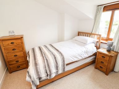 A bedroom with a single wooden bed between a wooden chest of drawers and a wooden bedside table at Lavender Cottage in South Zeal
