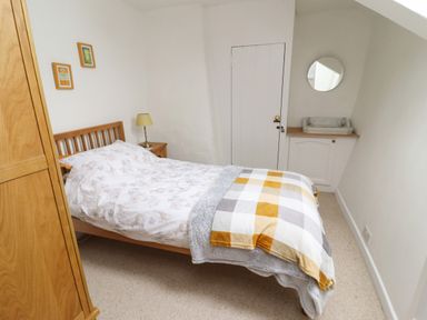 A bedroom with a double bed wooden wardrobe bedside table with lamp and a wash basin with mirror at Lavender Cottage South Zeal