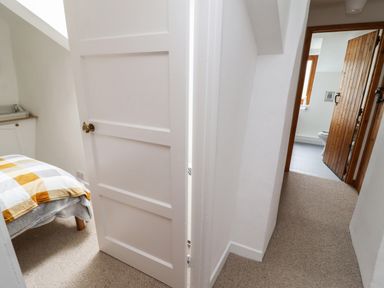 A hallway with carpet leading to a bedroom with a bed and a bathroom with a wooden door at Lavender Cottage in South Zeal